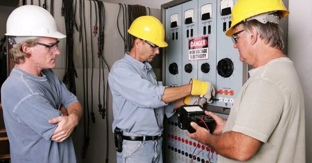 three men working on an industrial electrical board