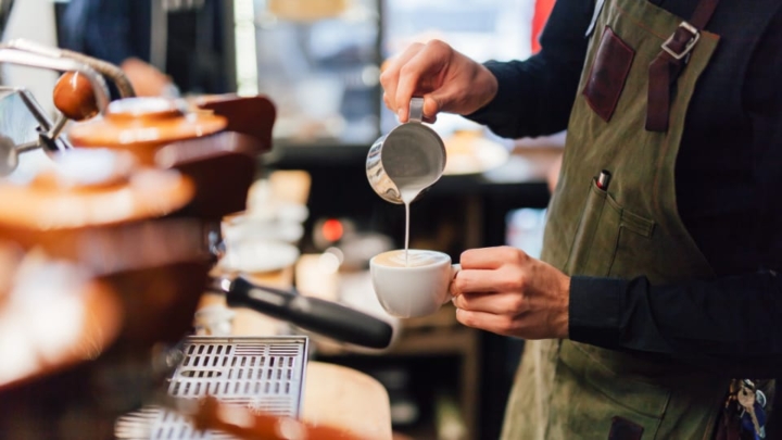 Barista pouring steamed milk onto a drink.