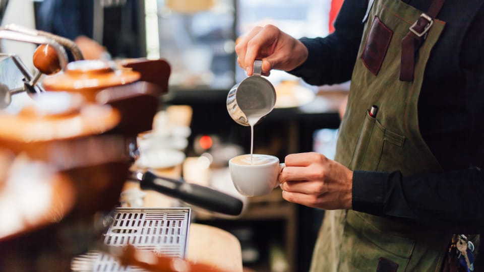 Barista pouring steamed milk onto a drink.